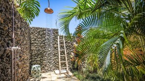 A stone-walled shower area with a ladder, a hanging showerhead, and a backpack on the floor. - Luxury 4 Bedroom with private pool & Spa (Waimea)