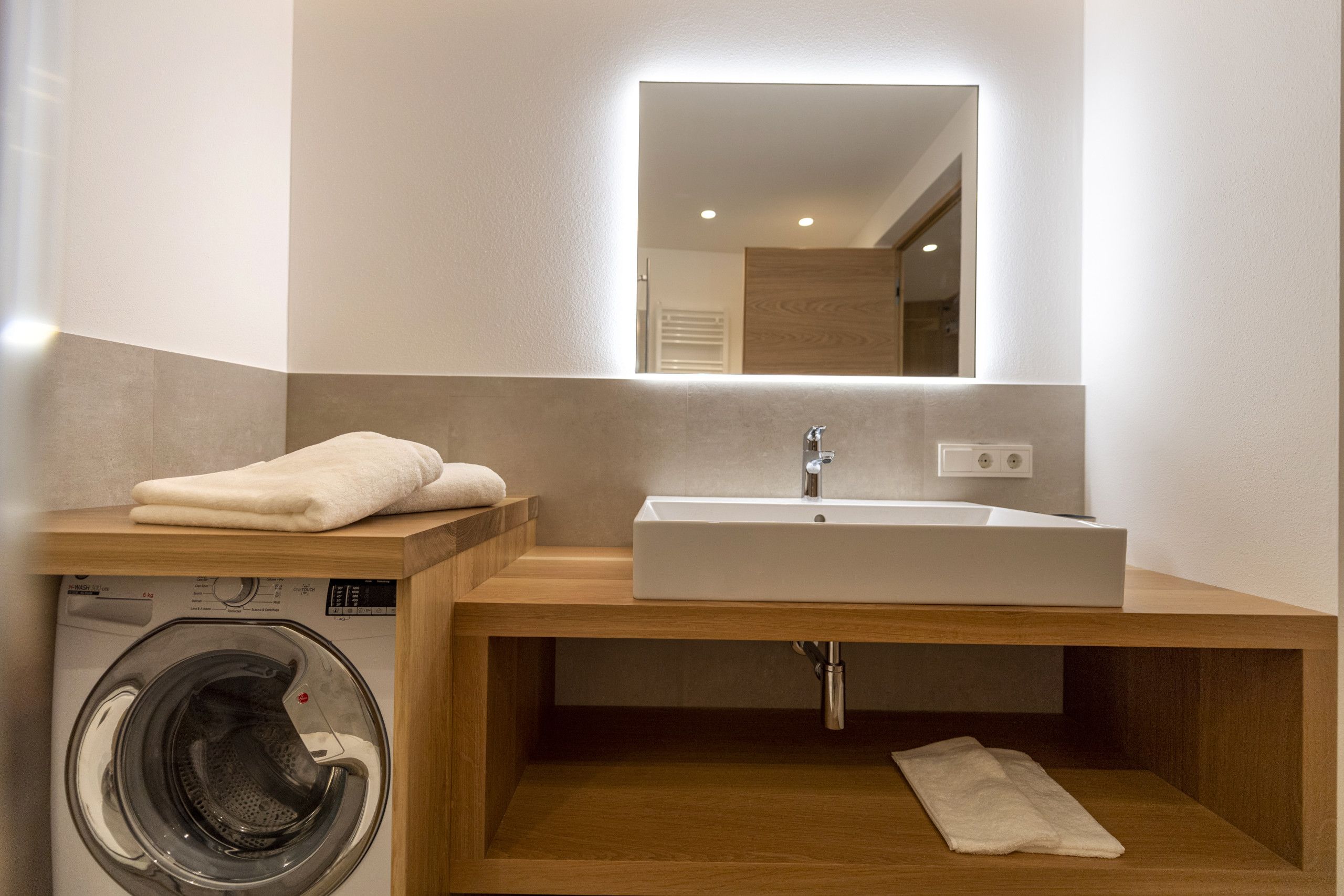 A modern bathroom with a built-in washing machine, a sink, and a mirror.