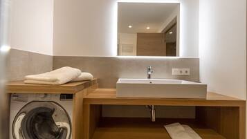 A modern bathroom with a built-in washing machine, a sink, and a mirror.