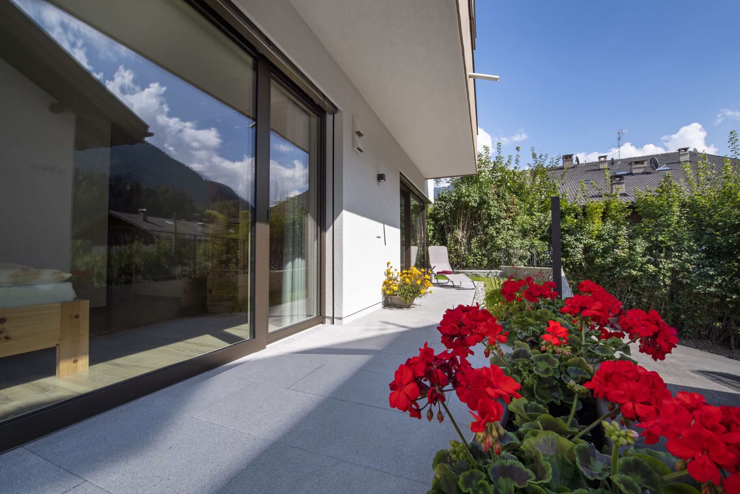 Ein modernes Haus mit großen Schiebegläsern, einer Holzbank und roten Blumen im Vordergrund.