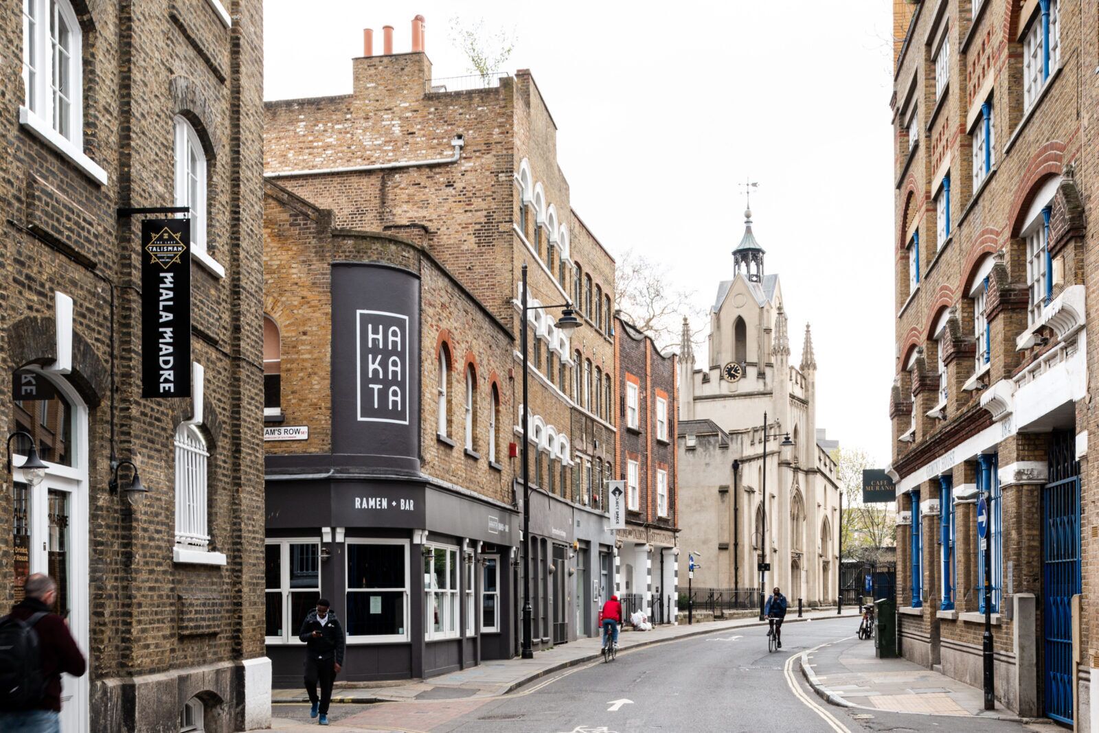 Une rue bordée d’immeubles, avec une église et une enseigne indiquant « Hakata ».