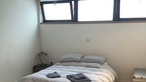 Um quarto com uma cama, mesa de cabeceira, luminária, janela e caixa organizadora.