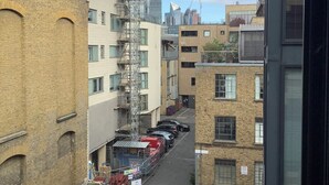 Uma rua estreita no centro da cidade, com edifícios altos, carros estacionados e andaimes de construção.