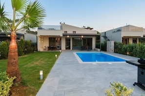 Une maison moderne dotée d’une piscine, d’un patio et d’une pelouse bien entretenue.