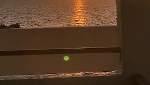 Ein Sonnenuntergang über dem Meer, betrachtet von einem Fenster mit Blick auf die See und den weiten Horizont.