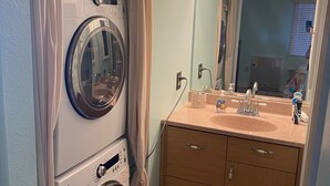 Ein kleines Badezimmer mit Waschmaschine, Waschbecken und Spiegel sowie einem Schrank.