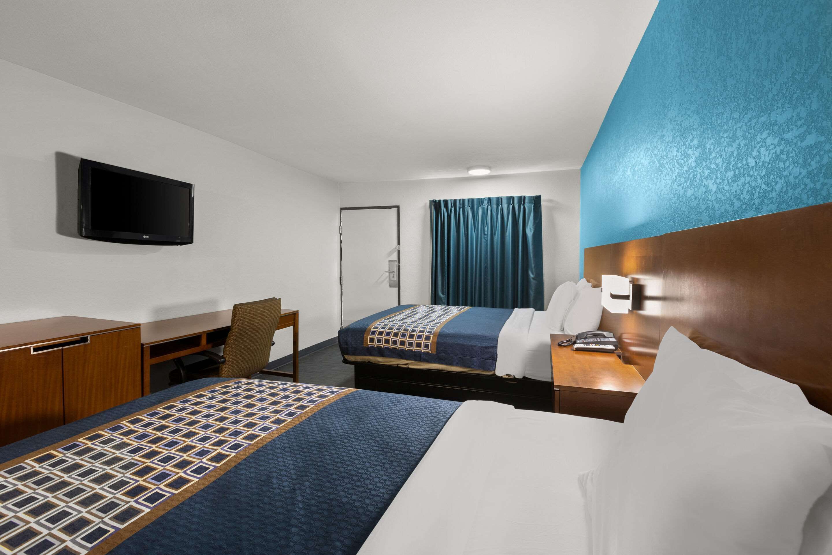 Habitación de hotel con dos camas, un escritorio, una silla, un televisor y la puerta del baño.