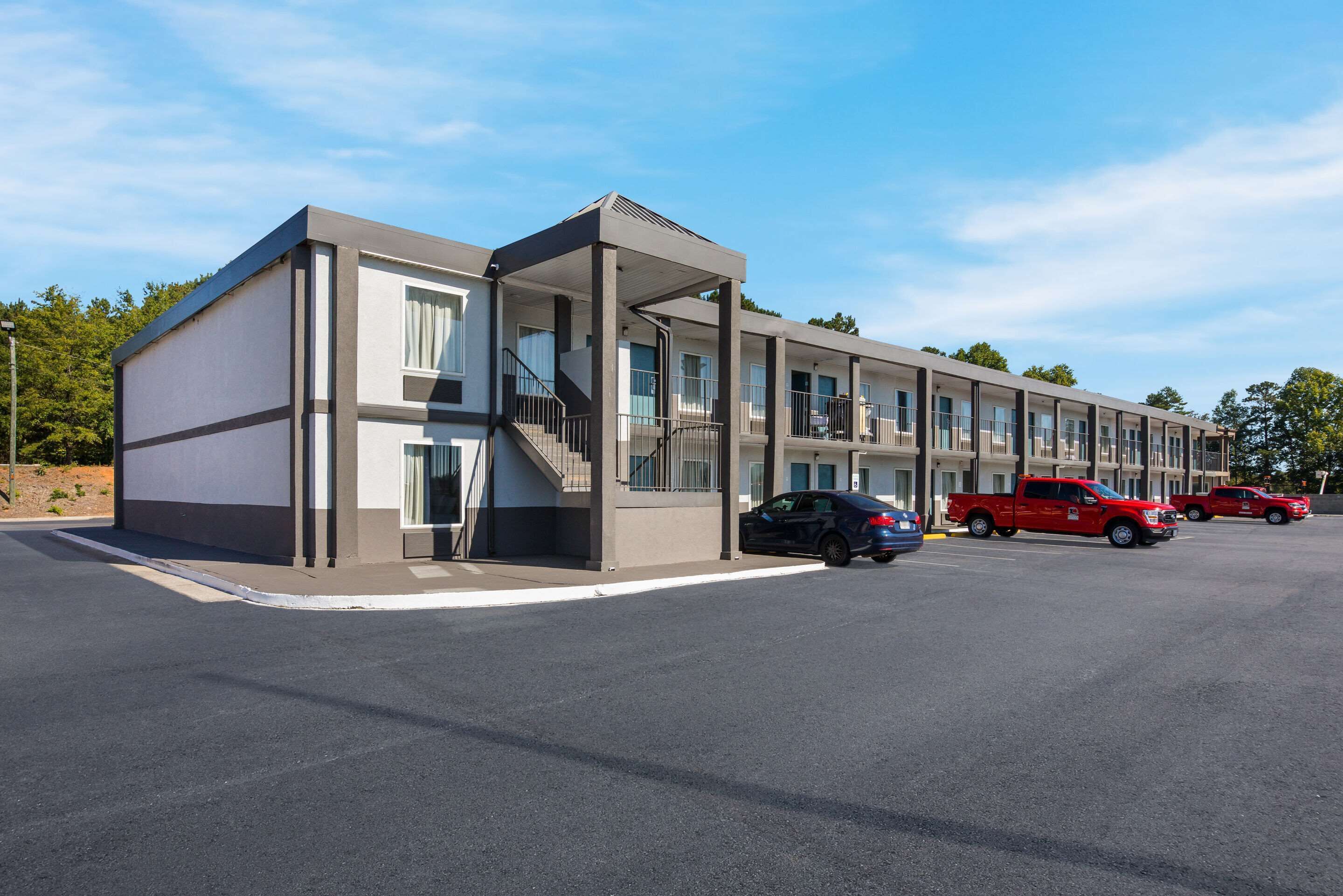 Un motel moderno con acceso cubierto, varias habitaciones y un estacionamiento con automóviles.