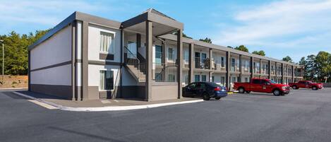 Un motel moderno con acceso cubierto, varias habitaciones y un estacionamiento con automóviles.