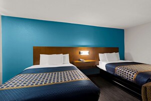 Habitación de hotel con dos camas, un cabecero de madera, una mesita de noche con teléfono e iluminación empotrada en la pared.