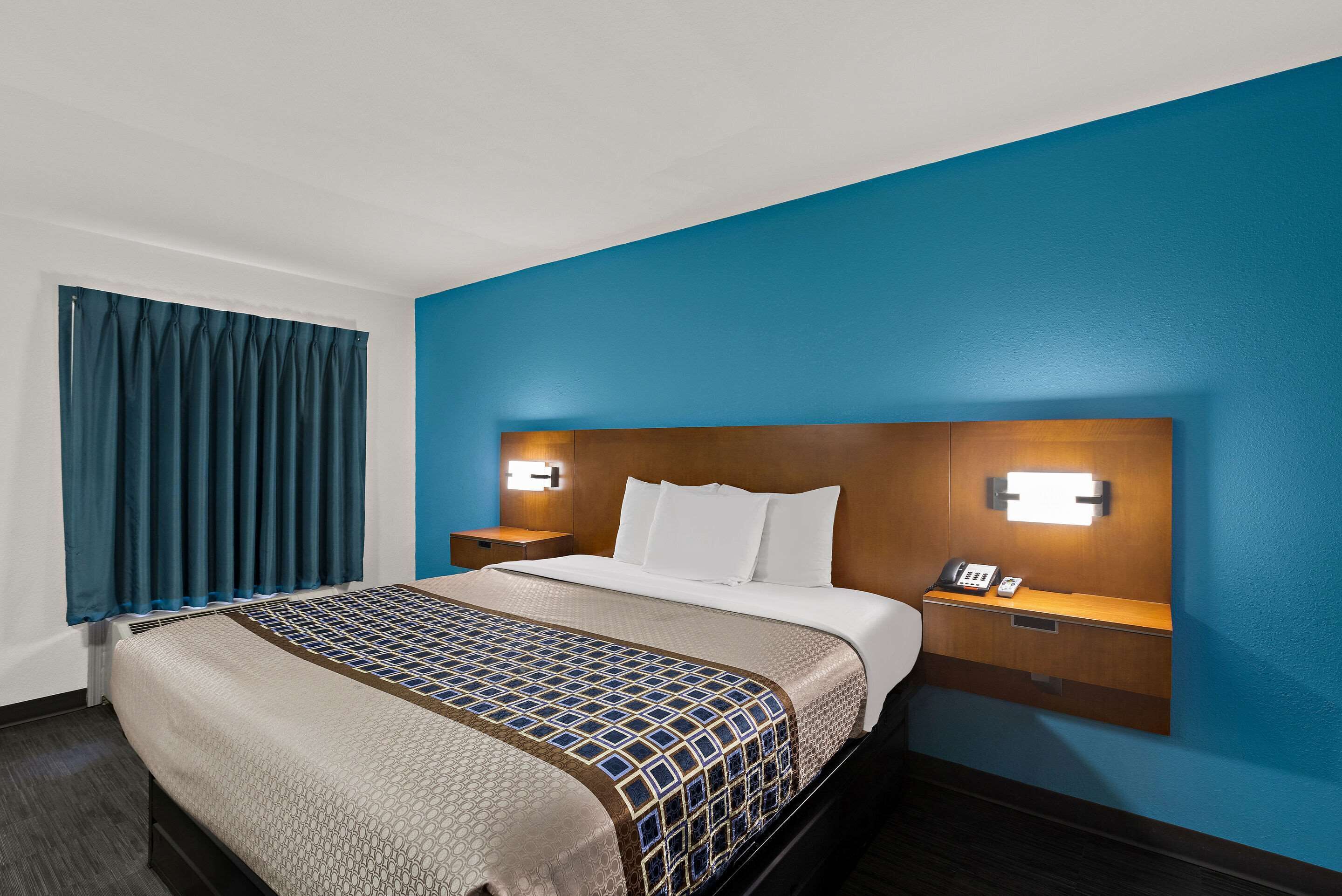 Una habitación de hotel con una cama grande, un cabecero de madera, mesitas de noche con lámparas y una pared azul decorativa.