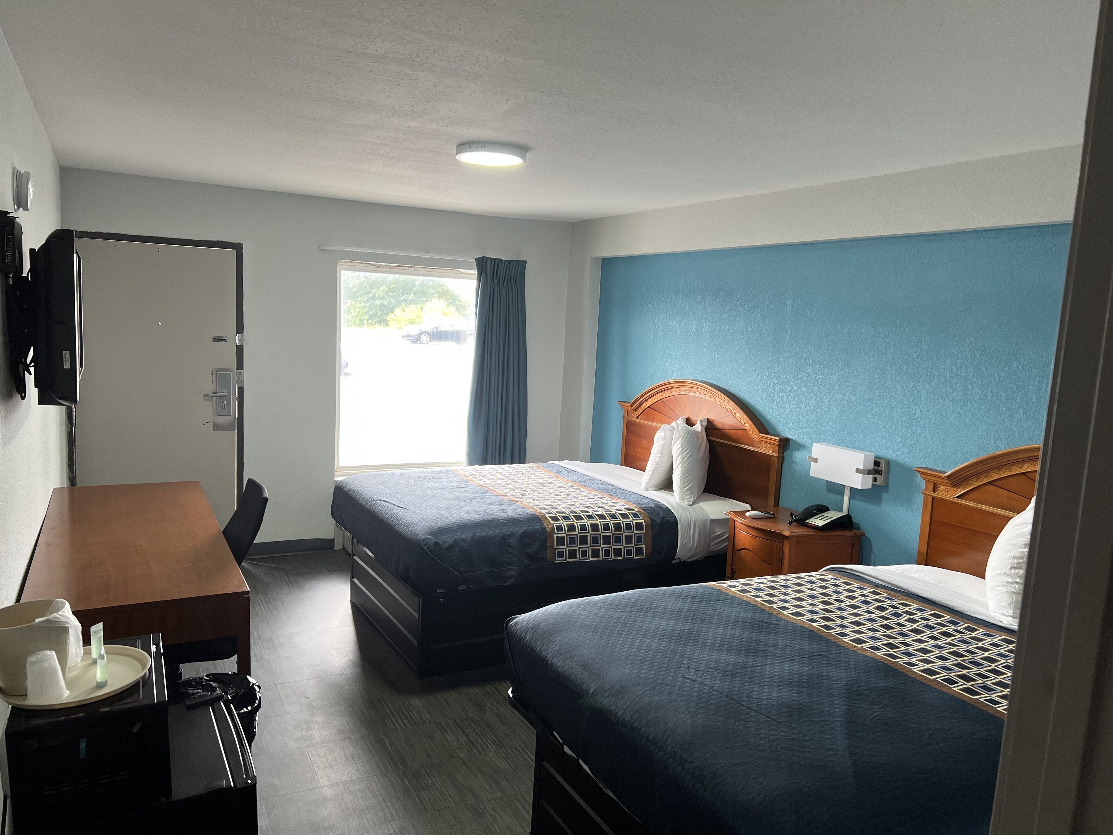 Une chambre d’hôtel avec deux lits, un bureau, une chaise, une télévision et une fenêtre avec des rideaux.