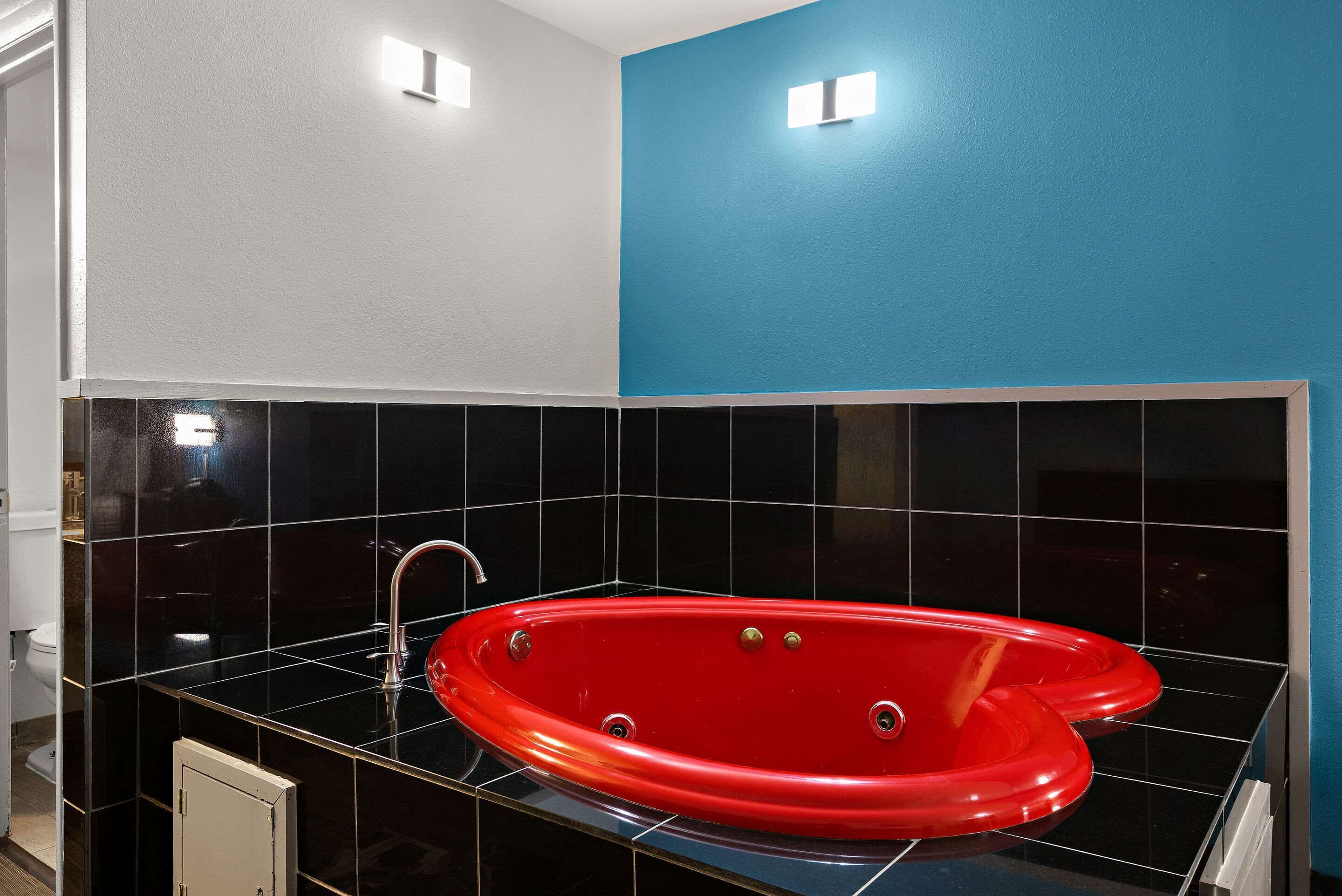 A bathroom with a red bathtub, black tiles, and a blue accent wall.