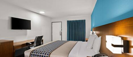 Ein Hotelzimmer mit einem Bett, einem Schreibtisch, einem Sessel, einem Telefon und einem an der Wand befestigten Fernseher.