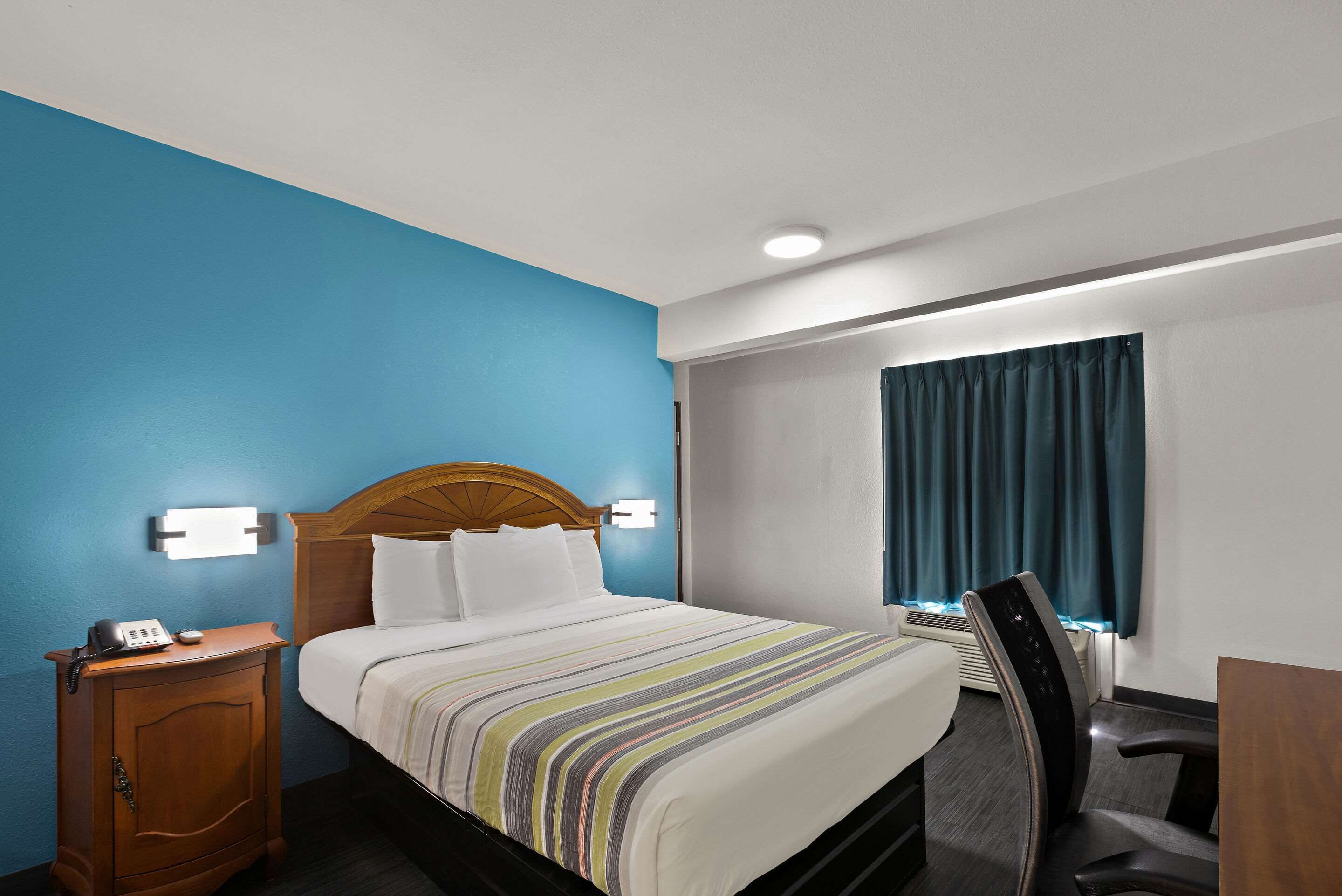 A hotel room with a bed, bedside table, and a desk with a chair.