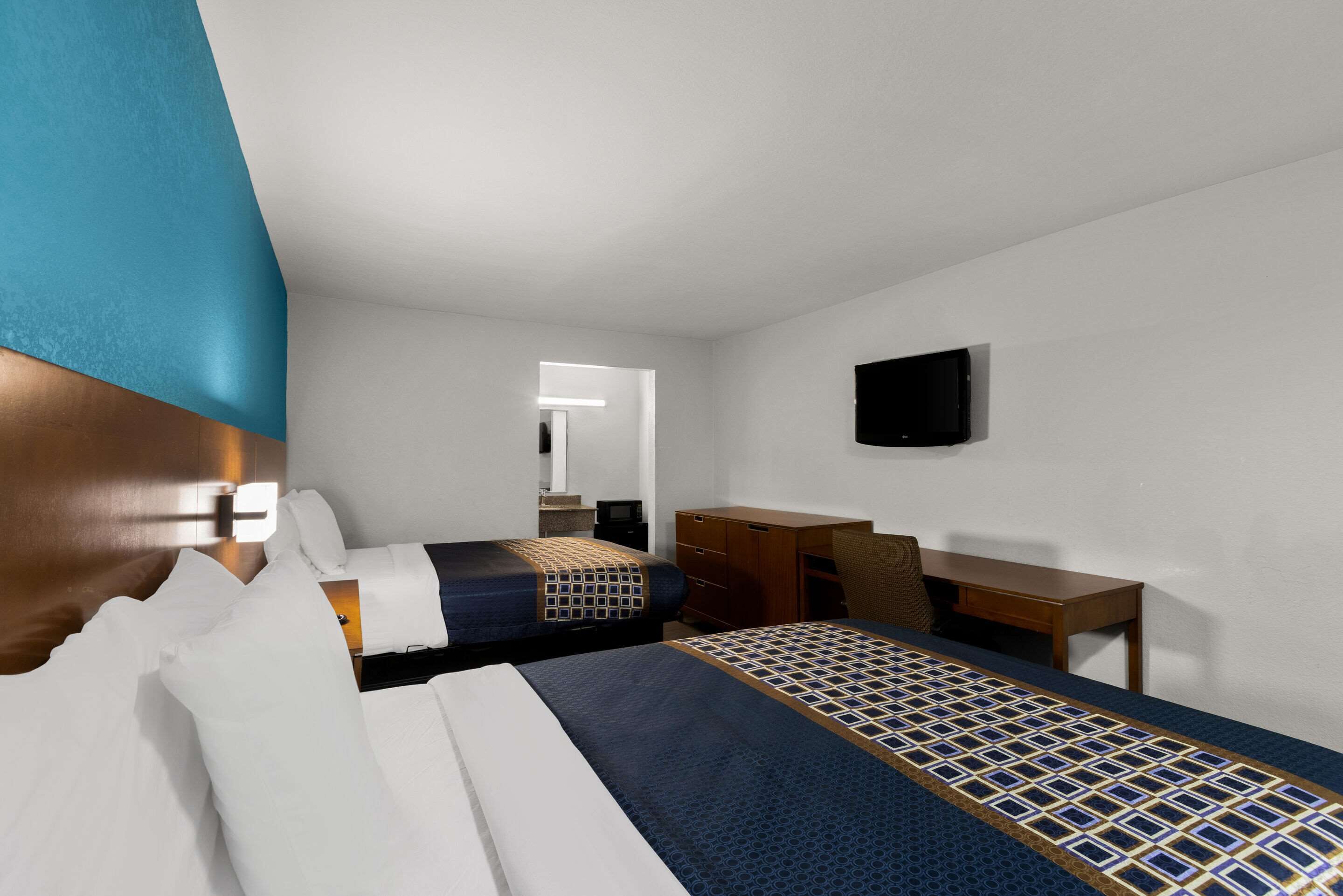 Habitación de hotel con dos camas, un escritorio, una silla, un televisor y un espejo.