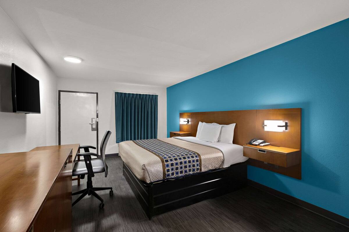 Une chambre d’hôtel comprenant un lit, une table de chevet, une lampe et un bureau avec une chaise.