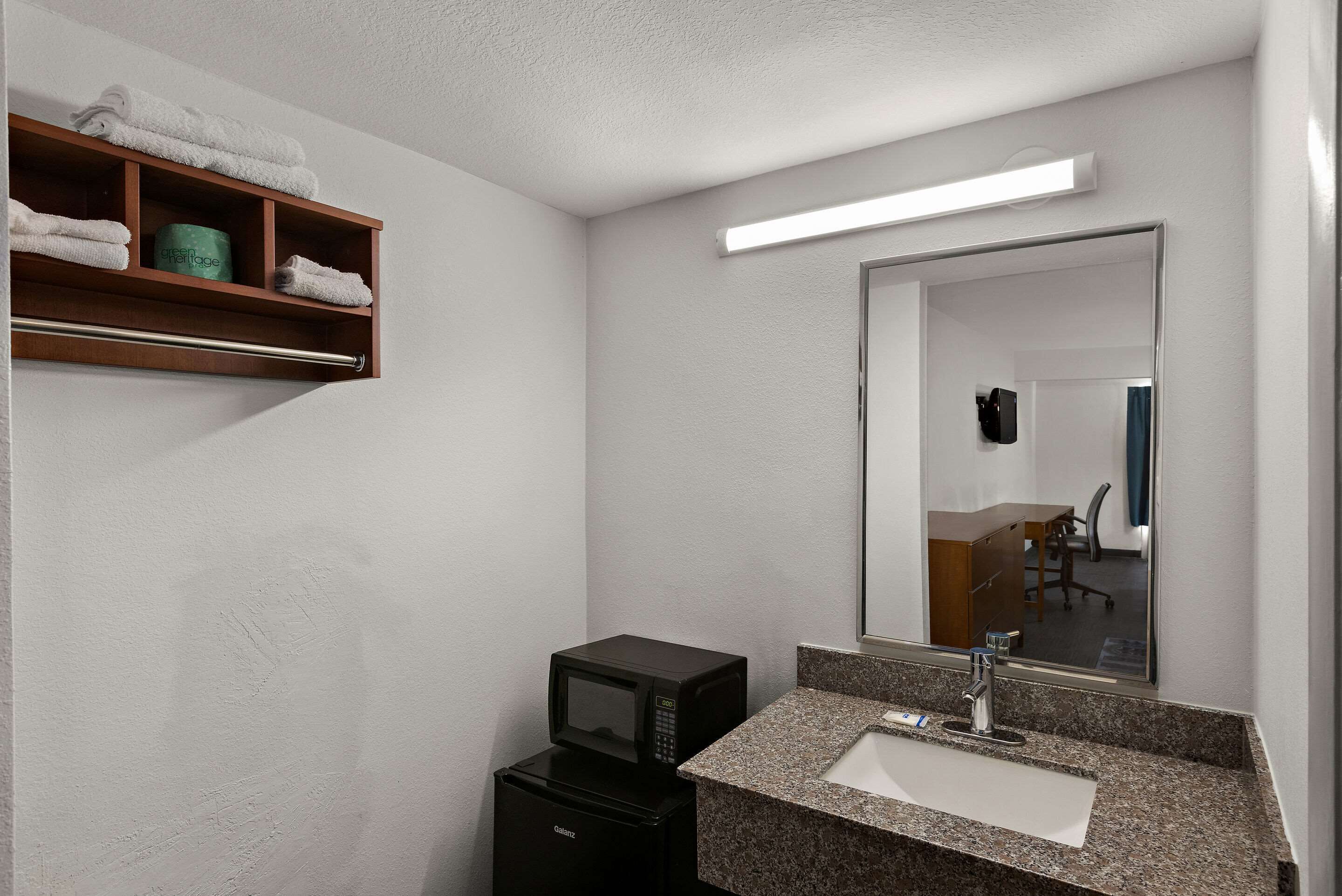 Un baño moderno con microondas integrado, un lavabo con encimera de granito y un espejo sobre el lavabo.