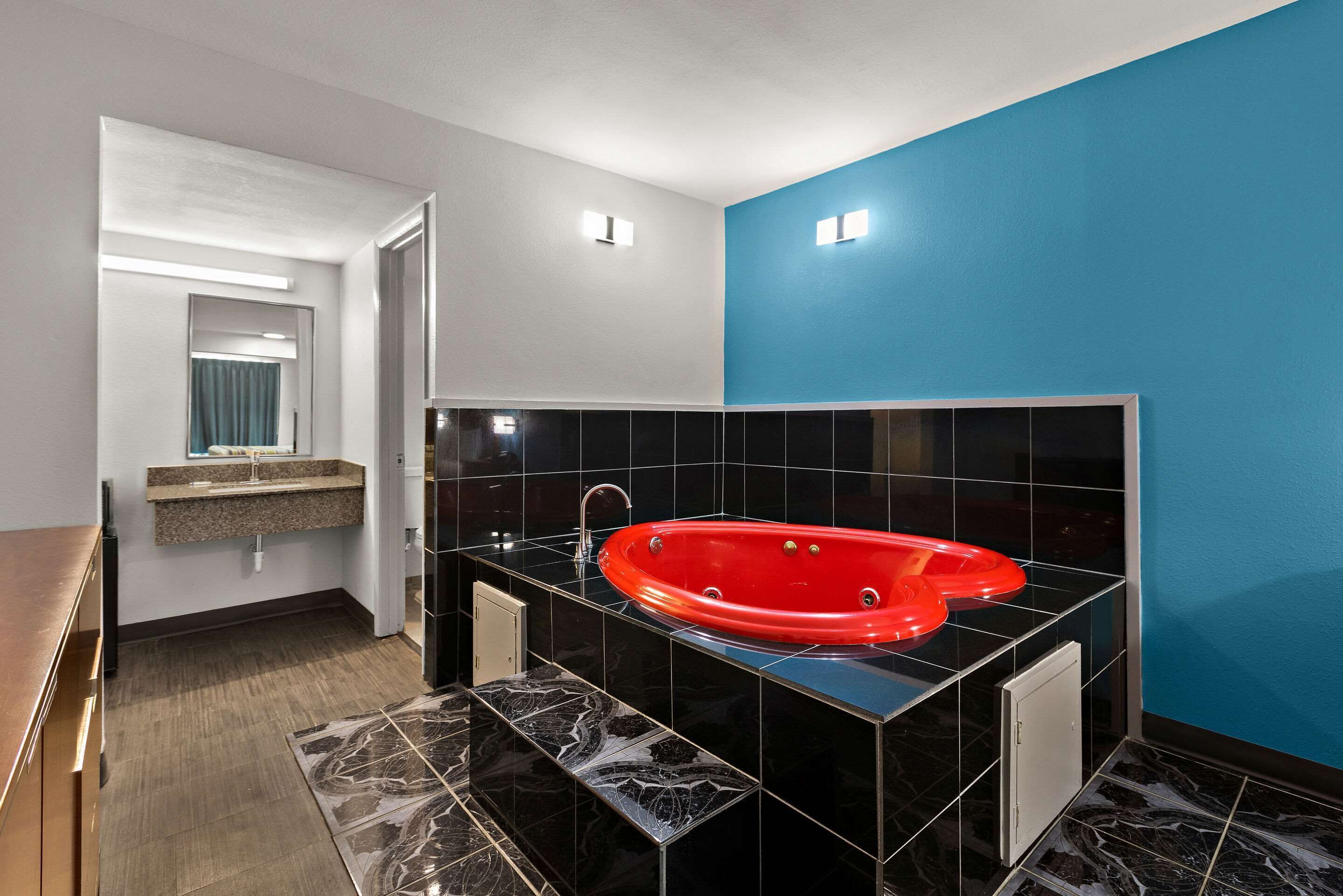 Une salle de bain moderne avec une baignoire noire et rouge, un meuble-lavabo avec un miroir et un mur d’accent bleu.