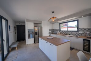 A modern kitchen with a central island, built-in appliances, and a large window providing natural light. - Spacious Luxury Villa with Pool – Walk to Beach – Ideal for Families or friends (Vaux-sur-Mer)