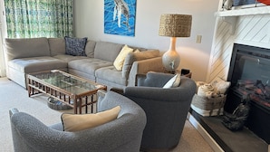 A living room with a sofa, armchair, glass coffee table, and a fireplace. - Superheat Retreat - Just 75 step to the beach. Breathtaking ocean view. (Kitty Hawk)