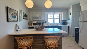 A kitchen with white cabinets, a central island with chairs, a microwave, stove, and a refrigerator. - Superheat Retreat - Just 75 step to the beach. Breathtaking ocean view. (Kitty Hawk)