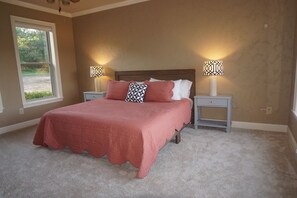 Un dormitorio con una cama grande, dos mesitas de noche con lámparas, una ventana y vistas al verdor exterior.