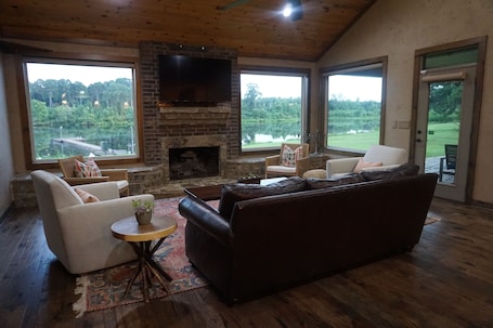 A cozy living room with a fireplace, comfortable seating, and large windows offering a view of the outdoors.