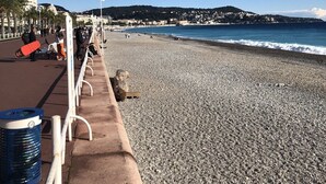 A pebbled beach with a concrete walkway, palm trees, and a flag. - Very cosy villa with swimming pool 20 minutes from Nice (Drap)
