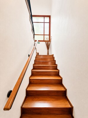 A wooden staircase with a handrail, a window with a view, and a door with an exit sign.