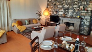 Uma sala de estar acolhedora com lareira de pedra, um sofá e uma mesa de jantar posta para uma refeição.