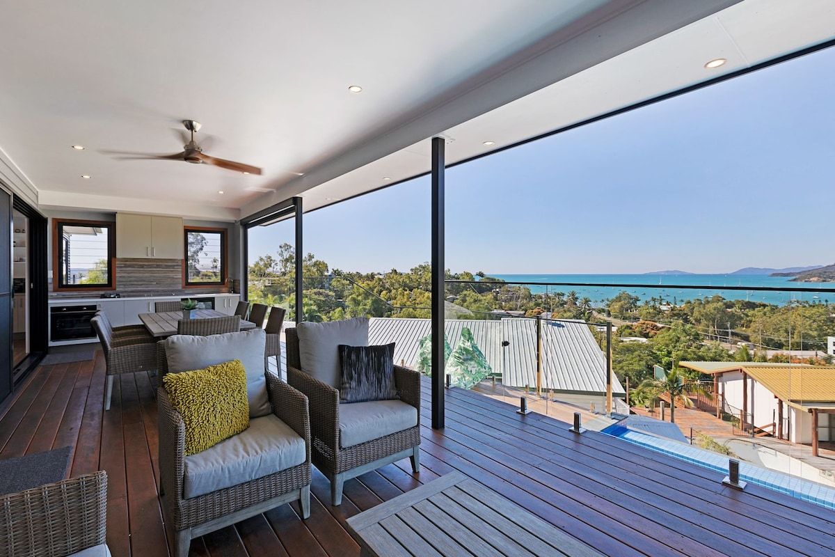 A balcony with wicker furniture, a ceiling fan, and a view of the sea and landscape.