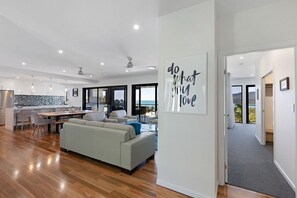 A modern living room with a sofa, dining area, and kitchen. There is a large window providing a view of the outdoors.
