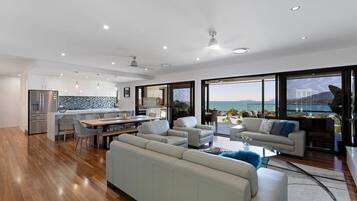 A modern living space with a kitchen, dining area, and seating area with a view of the sea.