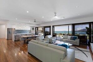 A modern living space with a kitchen, dining area, and seating area with a view of the sea. - Lux On Nara (Airlie Beach)