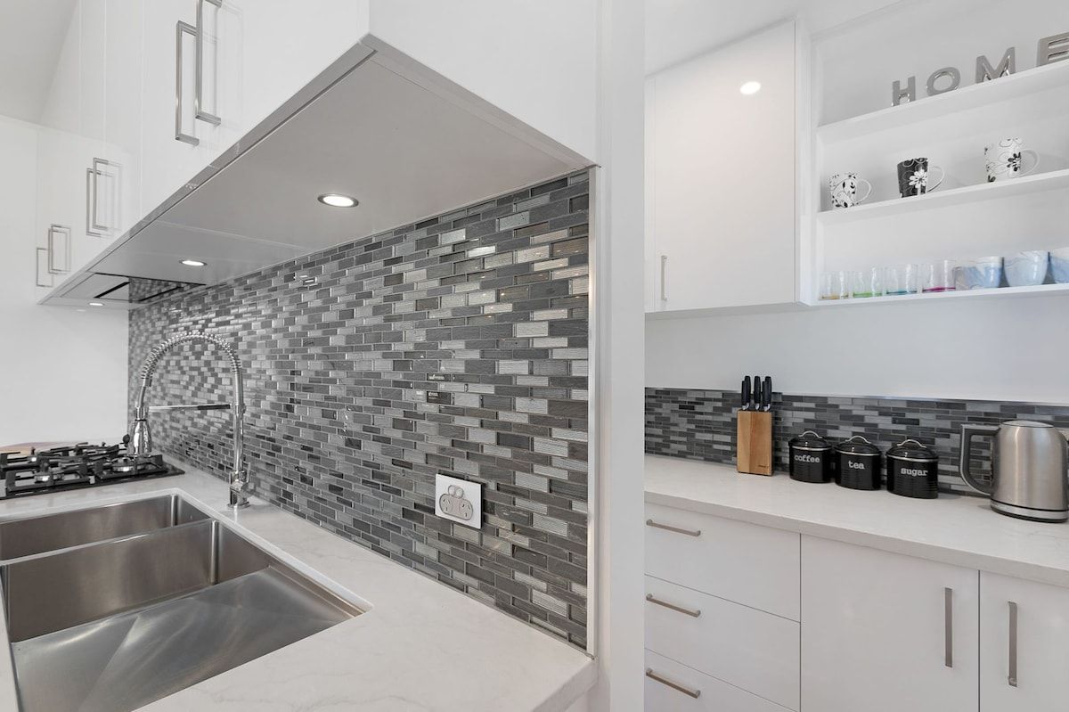 A modern kitchen with a tiled backsplash, stainless steel appliances, and a coffee station.