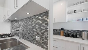 A modern kitchen with a tiled backsplash, stainless steel appliances, and a coffee station.