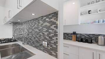 A modern kitchen with a tiled backsplash, stainless steel appliances, and a coffee station.