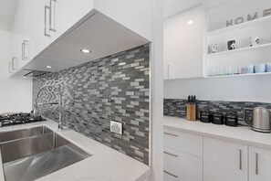 A modern kitchen with a tiled backsplash, stainless steel appliances, and a coffee station. - Lux On Nara (Airlie Beach)