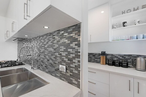 A modern kitchen with a tiled backsplash, stainless steel appliances, and a coffee station.