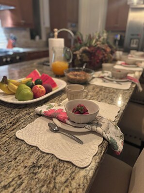 A kitchen counter with a fruit platter, a bowl of strawberries, and a coffee mug. - Sun Drenched Tuscan home! 4 Bedrooms 4.5 Bathrooms, 2 Primary Suites, 2 Bedrooms (La Quinta)