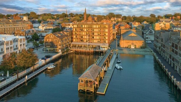 A riverside town with a prominent building featuring a large balcony and a dock extending into the water. - Wyndham Inn on the Harbor, perfect location (Newport)