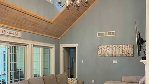 Uma sala de estar ampla com um sofá seccional grande, um lustre e vista para o exterior através de grandes janelas.