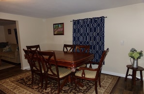 Un comedor con una mesa y sillas de madera, una alfombra estampada y una cortina azul.