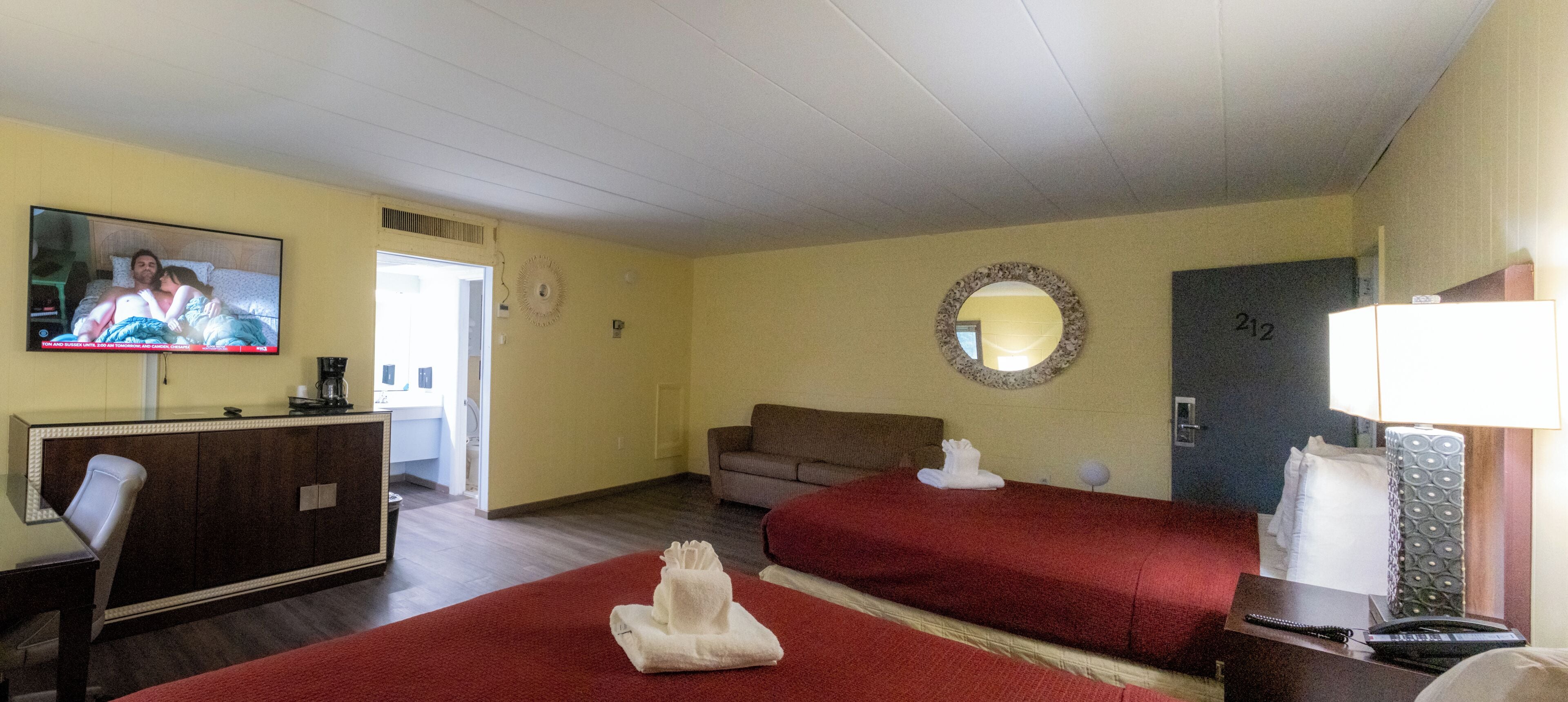 Habitación de hotel con dos camas, televisión, escritorio, espejo y puerta.