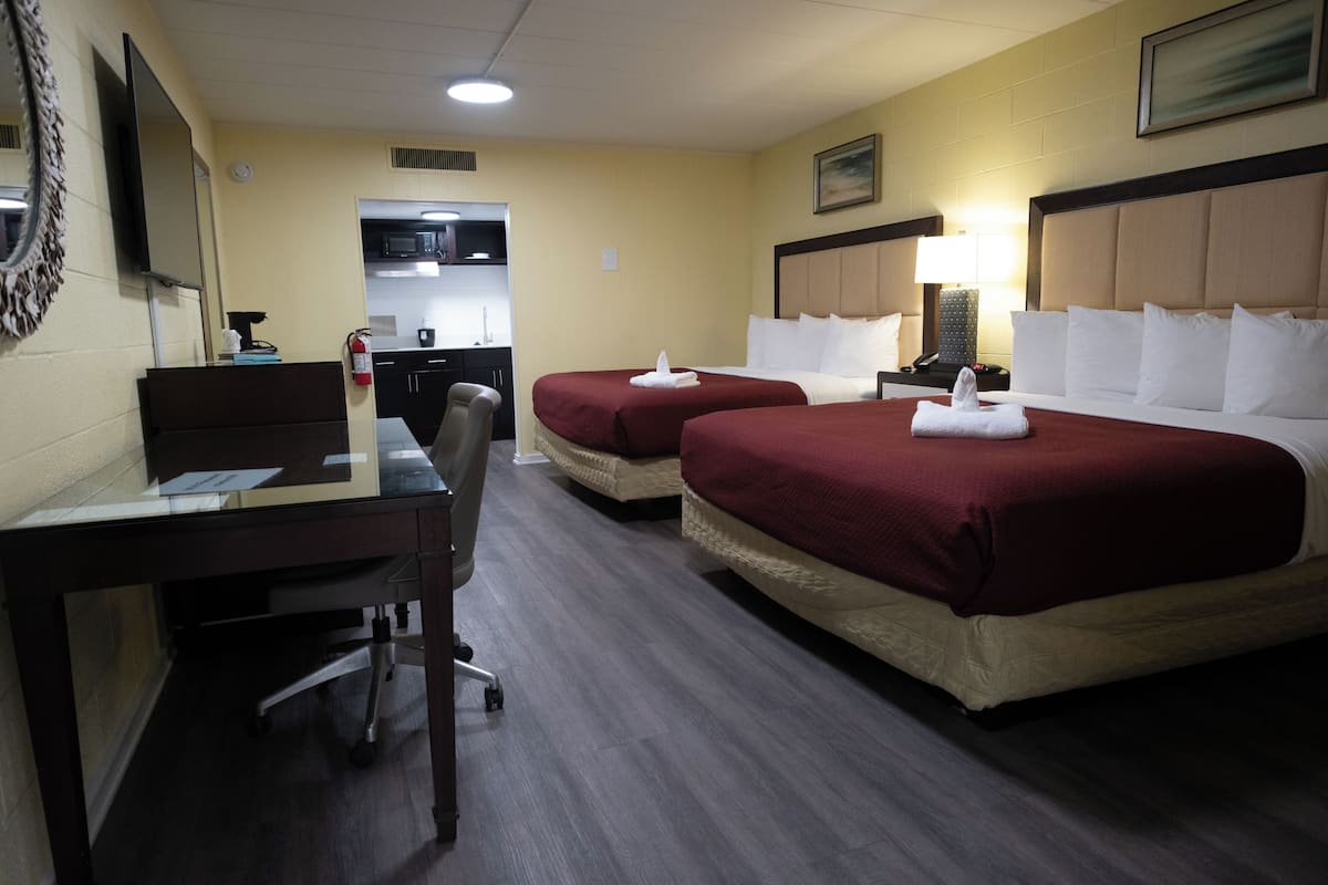 Ein Hotelzimmer mit zwei Betten, einem Schreibtisch, einem Sessel, einem Fernseher und einer Küchenzeile.