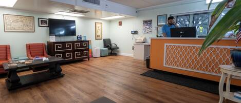 A reception area with a wooden floor, a reception desk, a television, and a chair.
