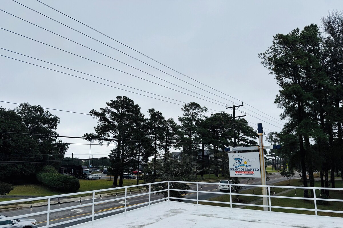 A view of a road with a white fence, trees, and a sign for 'Heart of Mantego Motor Lodge'.