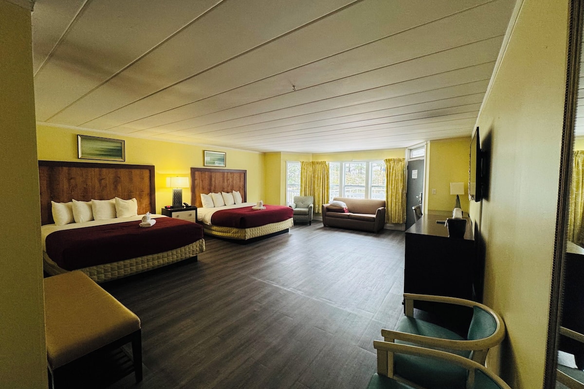 Ein Hotelzimmer mit zwei Betten, einem Schlafsofa, einem Sessel, einem Schreibtisch und einem Fernseher.