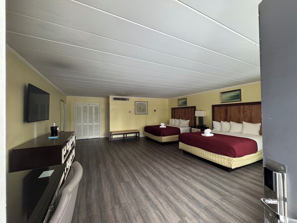 A hotel room with two beds, a desk, a chair, a TV, and a bench.